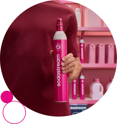 Mężczyzna trzyma nabój z CO2 Sodastream z szybkim złączem. Za nim widać sklepowe półki.